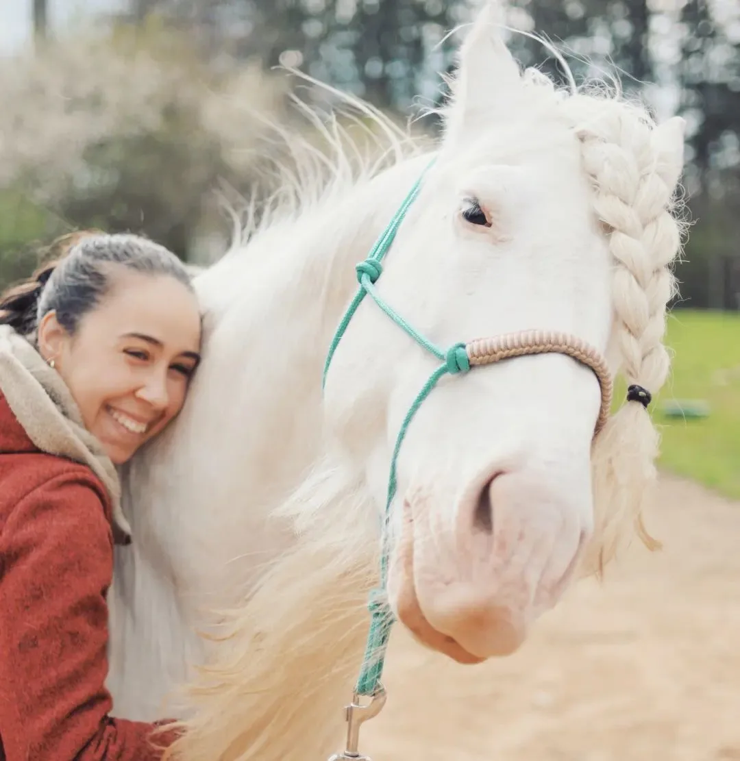 image of a person in a red coat hugging a white horse whose mane is braided.