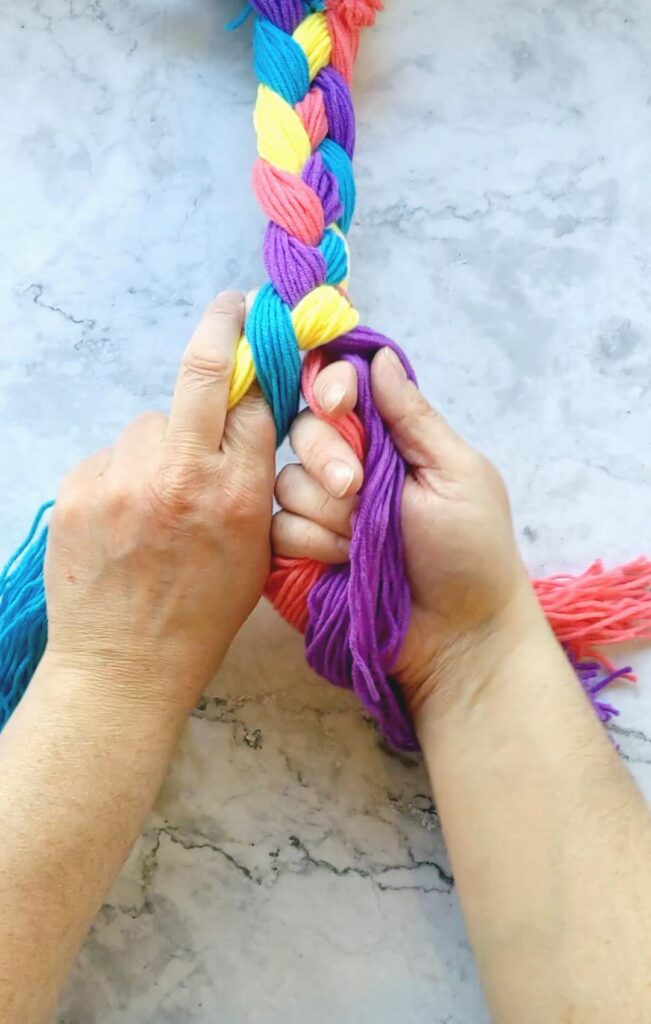 Hands holding and braiding 4 different colored groups of yarn.