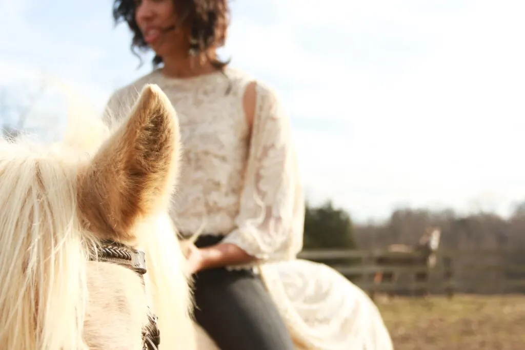 An out of focus woman on a white horse, only the ear of the horse is visible in the photo frame.