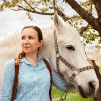 A smiling girl standing next to a white horse.
