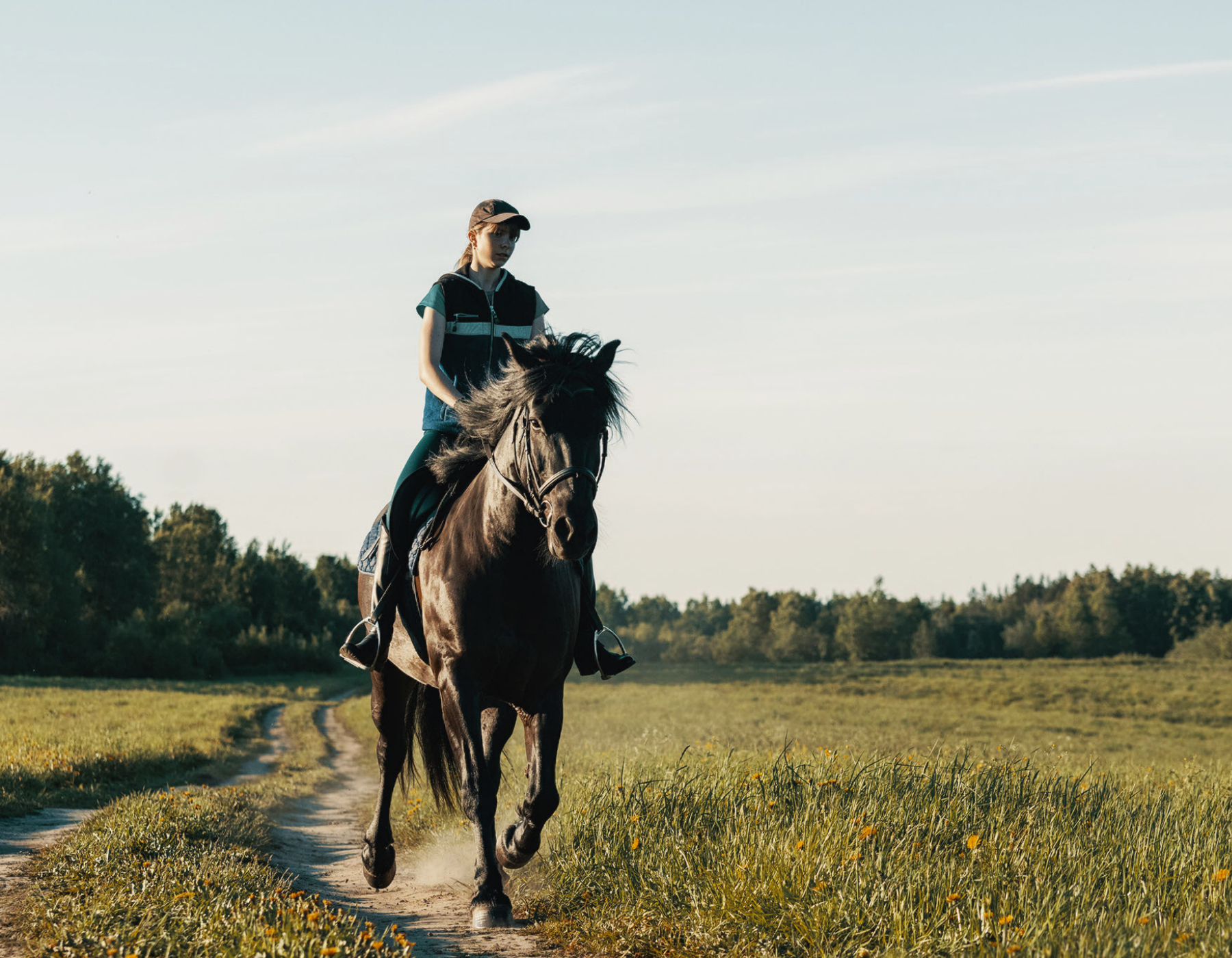 A teenage girl rides a free horse down a dirt path in a field.