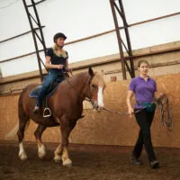 a horse, rider, and riding instructor in an airy indoor riding arena.
