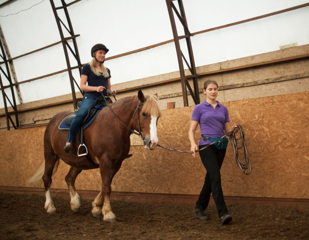 a horse, rider, and riding instructor in an airy indoor riding arena.