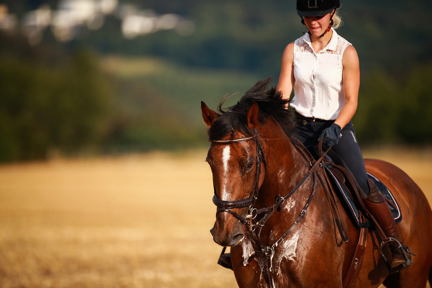 woman riding a brown horse that is covered in sweat.