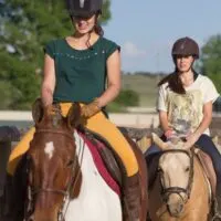 Two girls on horseback, riding near a fence.