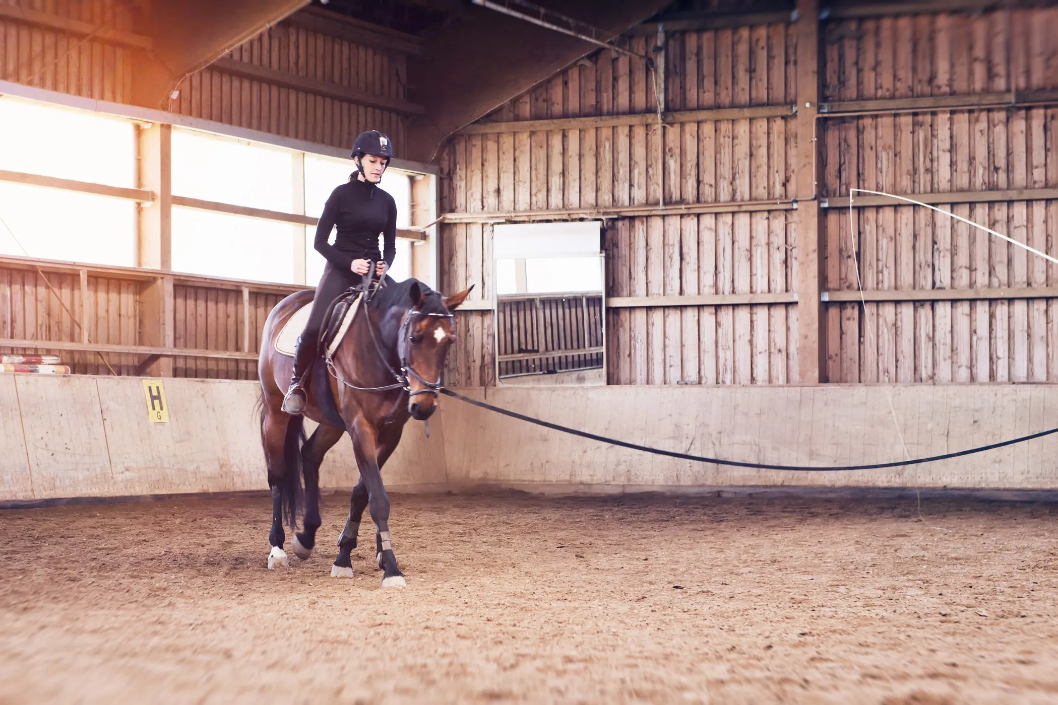 Young woman riding her horse in an indoor riding school on a lunging rein held by a riding lesson instructor