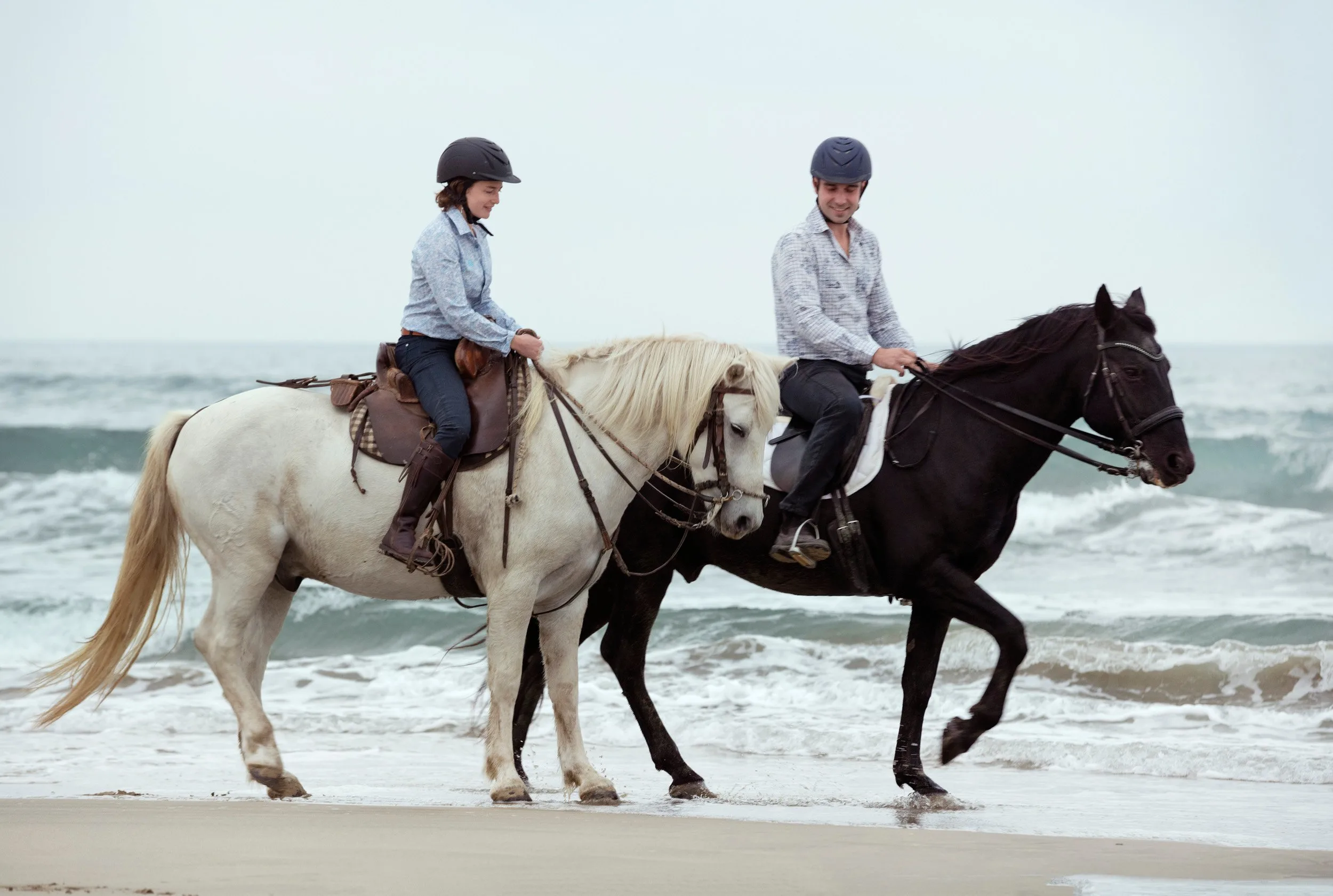 two riders riding their horses on the beach