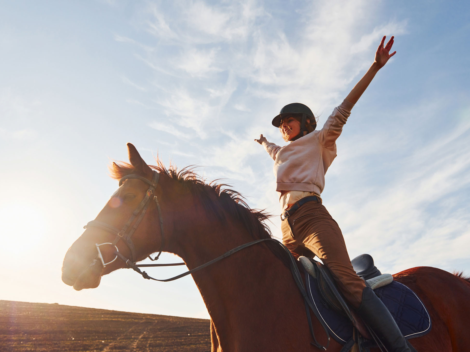 Woman on a brown horse with arms outstretched and smiling.