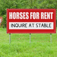 A sign advertising horses for rent in a horse pasture.