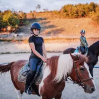 Two girls riding their horses outdoors at ranch.