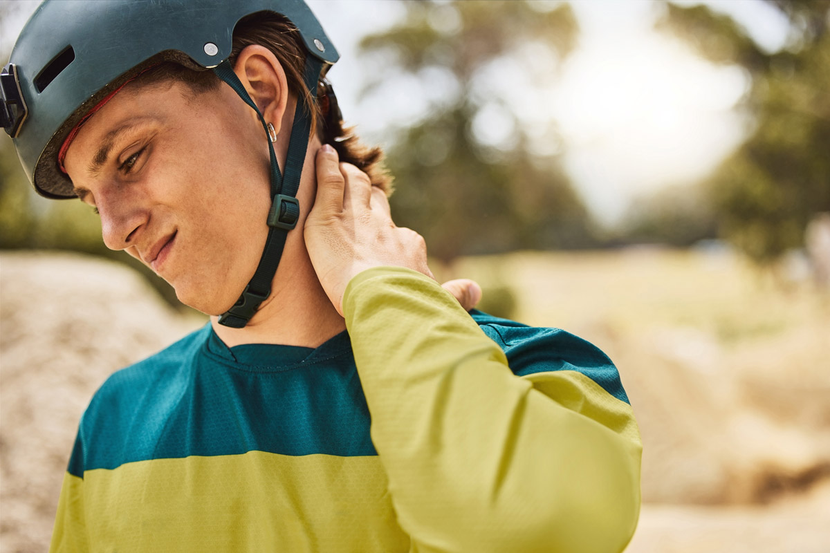 A person wearing a riding helmet rubs their neck while experiencing back pain