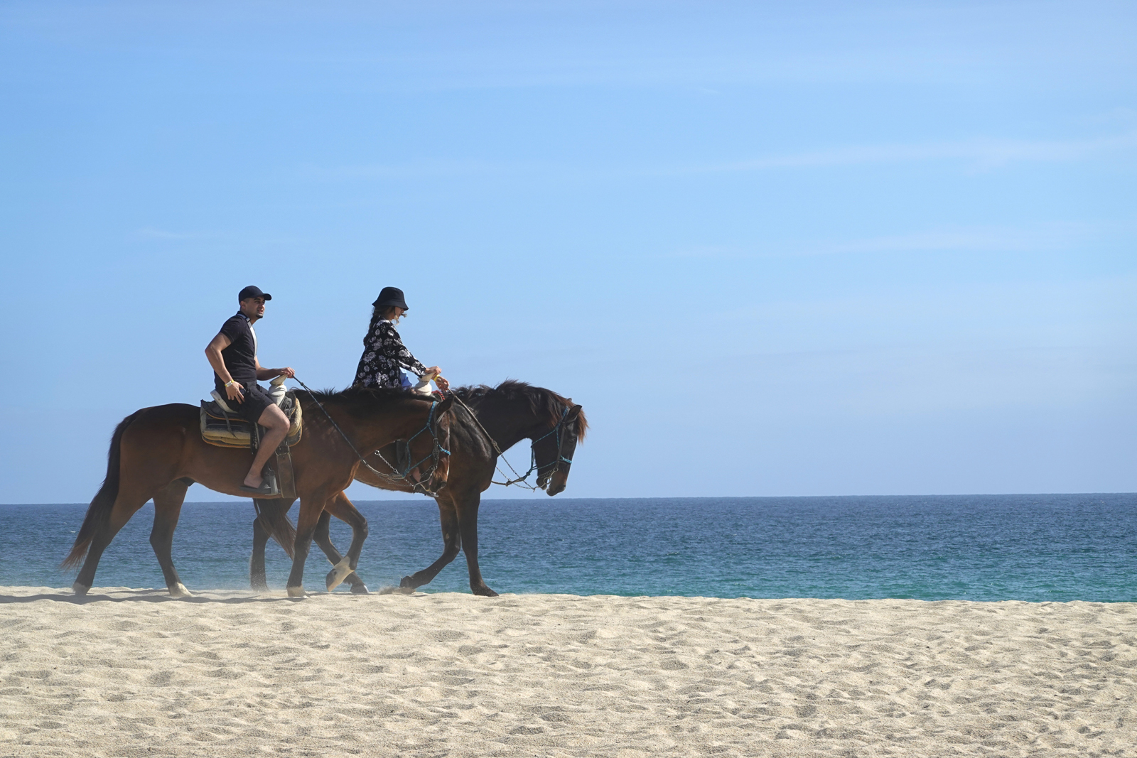 Two riders on horses on a coastal beach.