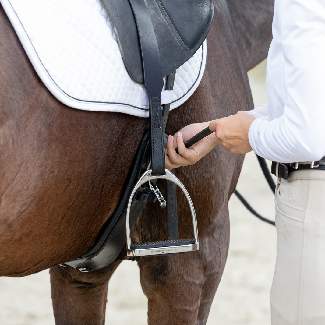 A rider tightens a piece of tack on a horse's saddle.